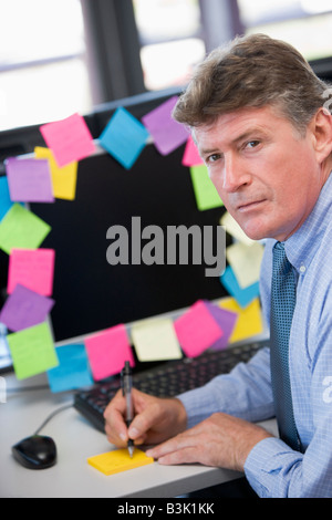 Businessman in office at monitor with notes on it writing Stock Photo