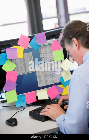 Businessman in office typing at computer with notes on it Stock Photo