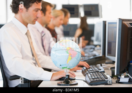 Five businesspeople in office space with a desk globe in foreground Stock Photo