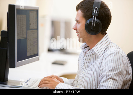 Man wearing headphones in computer room typing and smiling Stock Photo