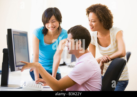 Three people in computer room pointing at monitor and smiling Stock Photo