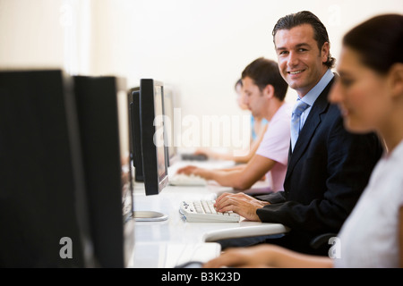 Four people in computer room with one man wearing a suit smiling Stock Photo