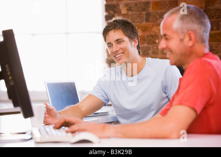 Two businessmen in office typing on computer and smiling Stock Photo