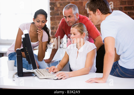 Four businesspeople in office space looking at computer smiling Stock Photo