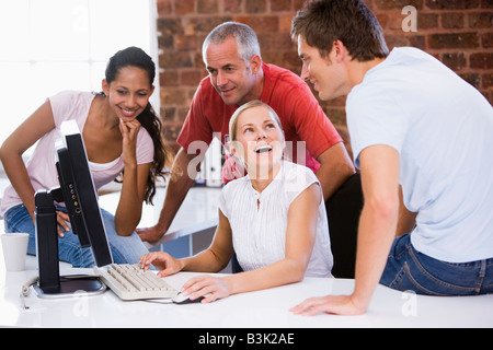 Four businesspeople in office space with computer smiling Stock Photo