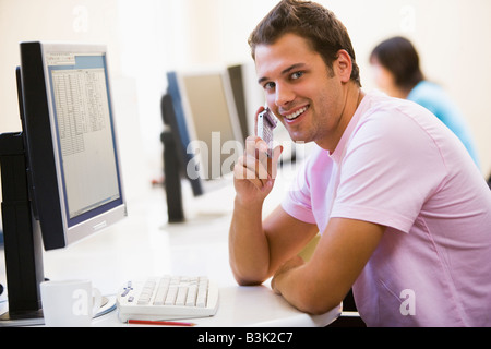 Man sitting in computer room using cellular phone and smiling Stock Photo