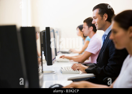 Four people sitting in computer room typing with one man in a suit Stock Photo