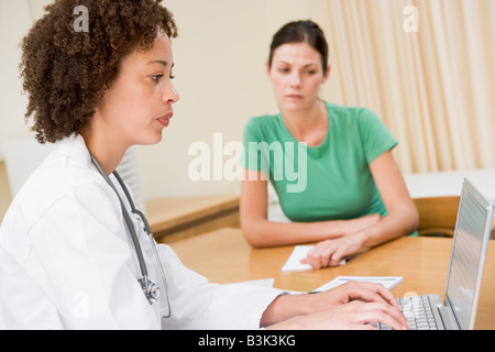Doctor using laptop with woman in doctor's office frowning Stock Photo