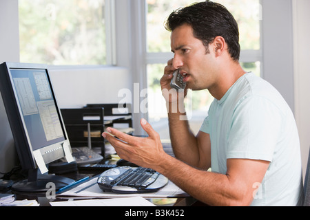 Man in home office on telephone using computer and frowning Stock Photo
