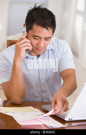 Man in dining room on cellular phone using laptop Stock Photo