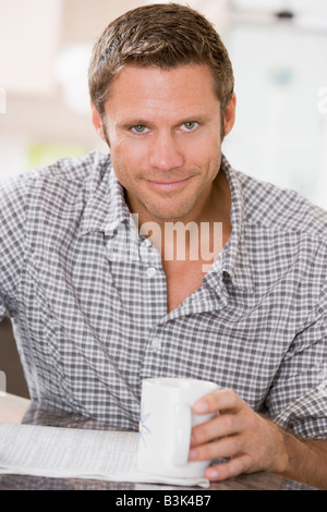 Man in kitchen reading newspaper and smiling Stock Photo