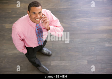 Businessman standing indoors using cellular phone smiling Stock Photo
