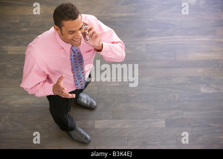 Businessman standing indoors using cellular phone smiling Stock Photo