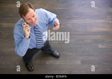 Businessman standing indoors using cellular phone and smiling Stock Photo