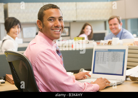 Businessman in cubicle using laptop and smiling Stock Photo