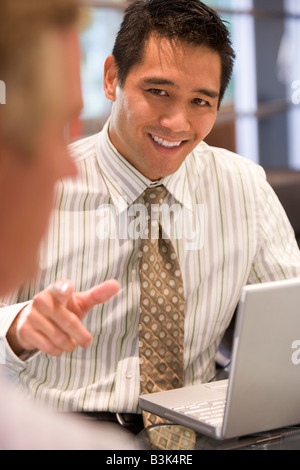 Two businessmen in boardroom with laptop talking Stock Photo