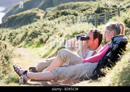Couple on cliffside outdoors using binoculars and smiling Stock Photo