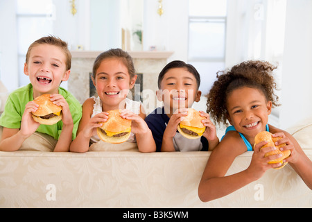 Four young children eating cheeseburgers in living room smiling Stock Photo