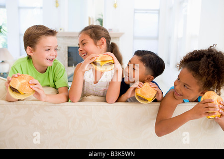 Four young children eating cheeseburgers in living room smiling Stock Photo