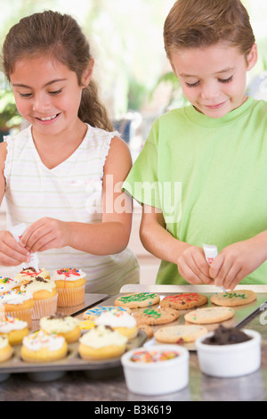 Two children in kitchen decorating cookies smiling Stock Photo