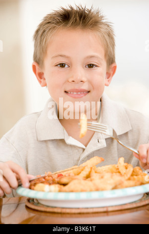 Young boy indoors eating fish and chips smiling Stock Photo