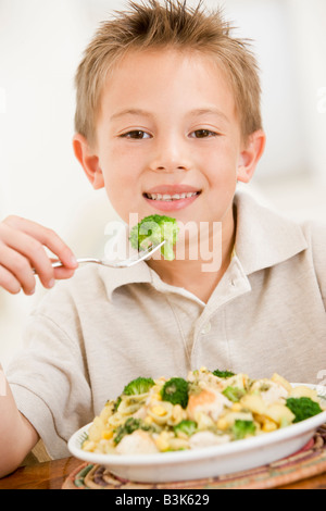 Young boy indoors eating pasta with brocolli smiling Stock Photo