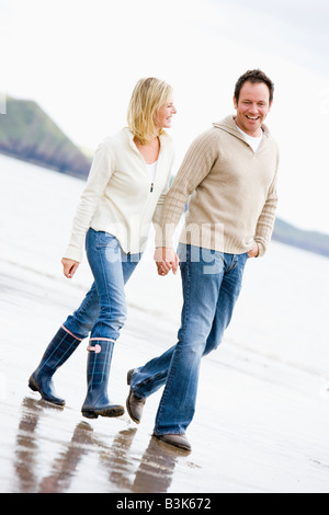 Couple walking on beach holding hands smiling Stock Photo