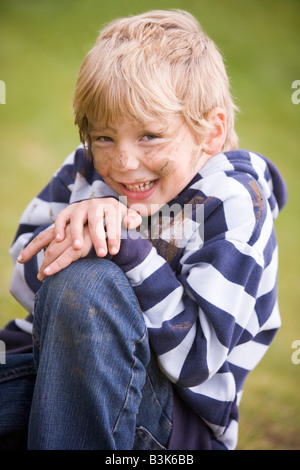 Young boy sitting outdoors dirty and smiling Stock Photo