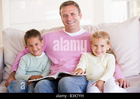 Man and two children sitting in living room reading book and smiling Stock Photo