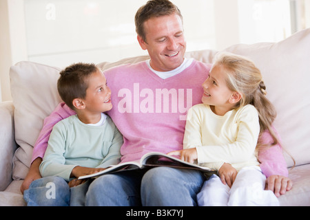 Man and two children sitting in living room reading book and smiling Stock Photo