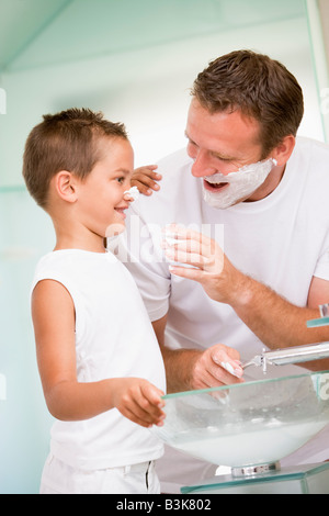 Man in bathroom putting shaving cream on young boy's nose Stock Photo