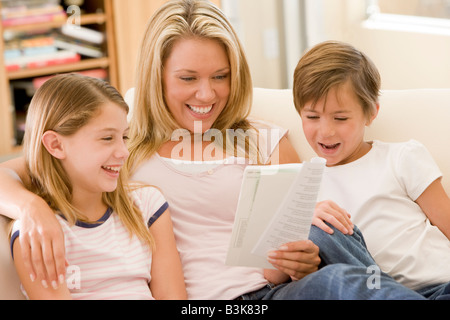 Woman and two young children in living room reading book and smiling Stock Photo