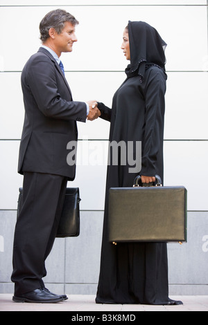 Two businesspeople outdoors shaking hands and smiling Stock Photo