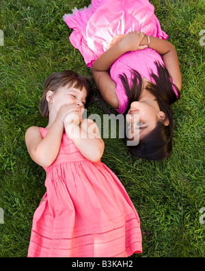 A little caucasian girl and an Indian girl lay in the grass to relax and play. Stock Photo