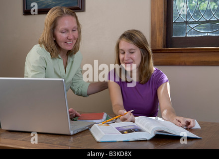 A mother helps her teen-aged daughter with school homework with a laptop computer on the table. Perhaps they are using the wifi Stock Photo