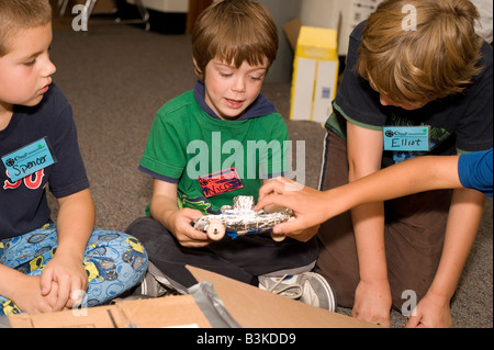 children showing each other vehicles made from recycled cardboard and plastic bottles in classroom Stock Photo