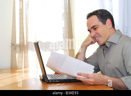 Man sitting at his desk with a laptop and papers looking happy Stock Photo