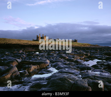 First sunlight of the day breaks over Dunstanburgh Castle Northumberland United Kingdom Stock Photo