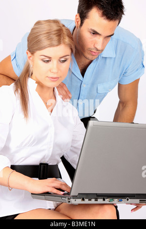 Young Man And Woman Working Business Partners Studying A Laptop Computer On The Woman's Lap Isolated Against A White Background With A Clipping Path Stock Photo
