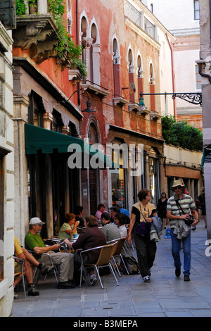 Venetian street scene showing ancient architecture and a typical cafe with outdoor seating and people walking Stock Photo
