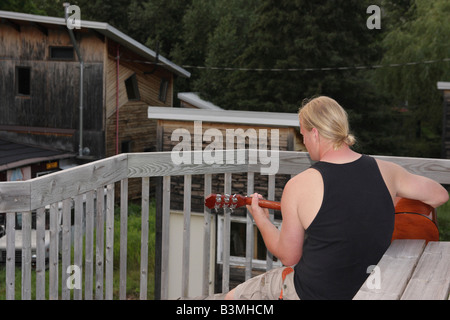 The Caucasian young man with blond hair playing on acoustic guitar rear view pictures images photos horizontal in USA US hi-res Stock Photo