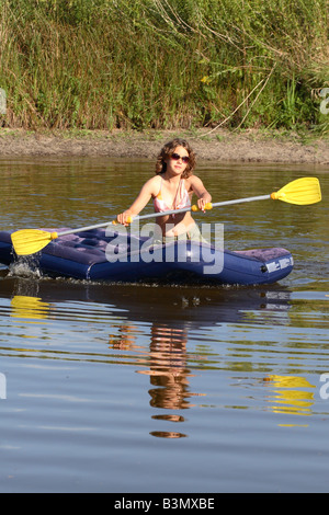 Teenage girl on an inflatable raft paddling across a small lake in the summer evening Stock Photo