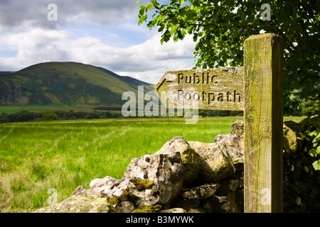 Wooden public footpath signpost sign and dry stone wall overlooking Lake District mountains in Cumbria, England, UK Stock Photo