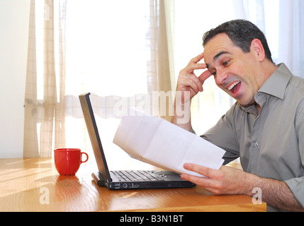 Man sitting at his desk with a laptop and papers looking happy Stock Photo