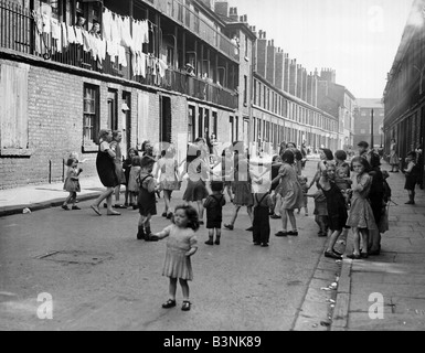 Children growing up in this poor street are accustomed to squalor but enjoy their games skipping swinging on lamp post and ring Stock Photo