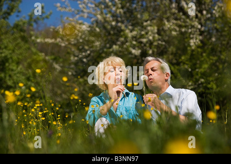 Germany, Baden Württemberg, Tübingen, Senior couple blowing on dandelions in meadow, portrait Stock Photo
