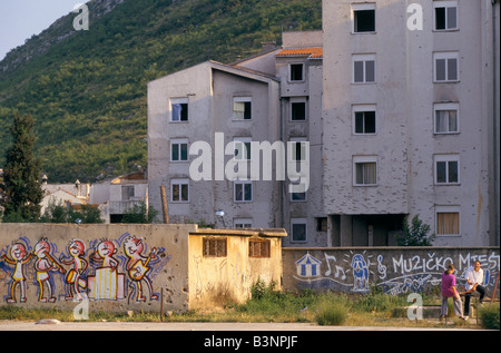 Mostar, june 1996', children playing on a seesaw in a playground next to buildings peppered with bullet marks, 1996 Stock Photo