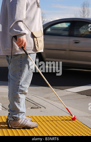 Blind woman standing on crosswalk platform as a car speeds by Stock Photo