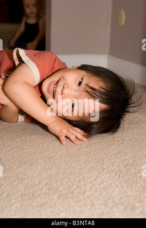 happy Japanese two year old boy lays on the floor while playing hide and seek Stock Photo