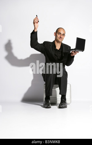 Man in a busines suit sat on a brief case lap top on knee holding a telephone Stock Photo